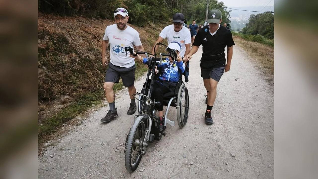 Un grupo de personas acompaña a un niño en una silla adaptada por un camino.
